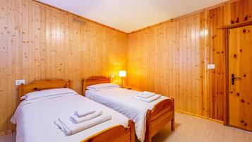Una habitación con dos camas de madera, una mesita de noche, una lámpara de pared y un armario de madera.