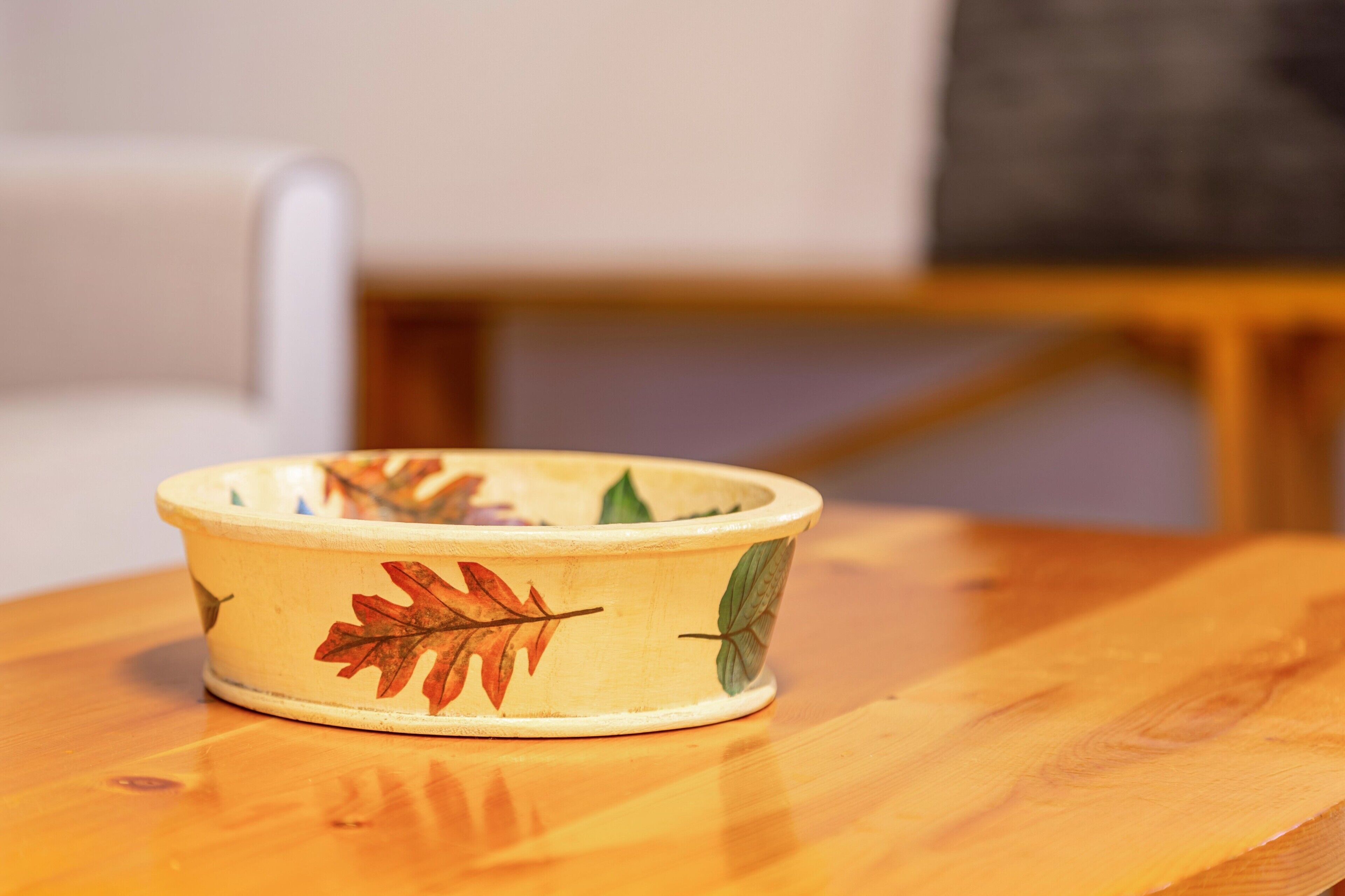 Een houten tafel met een keramieken kom met bladmotieven.
