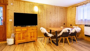 Una habitación con paneles de madera, una televisión, una mesa de comedor de madera, sillas y un vehículo blanco.