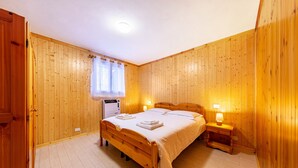 Una habitación con paneles de madera, una cama, mesitas de noche y un ventanal con cortinas.