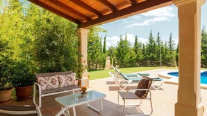 Un espace extérieur aménagé, abrité et doté de sièges, avec une piscine, le tout entouré d’arbres et de verdure.
