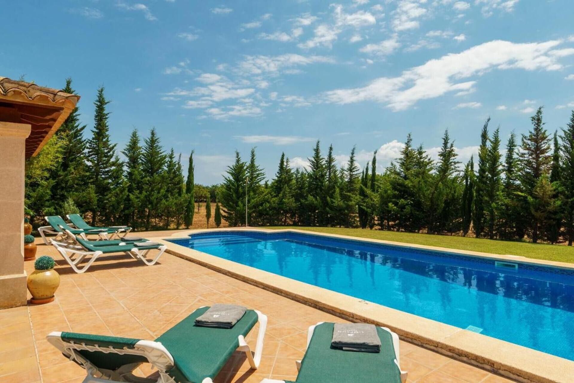 Una piscina con sillones de descanso, rodeada de árboles.