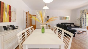 Un coin repas avec une table blanche, des chaises et un vase contenant des plantes séchées.