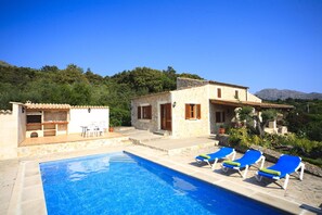 Un espace piscine avec des chaises longues, un petit bâtiment doté d’une terrasse et un paysage montagneux en arrière-plan.