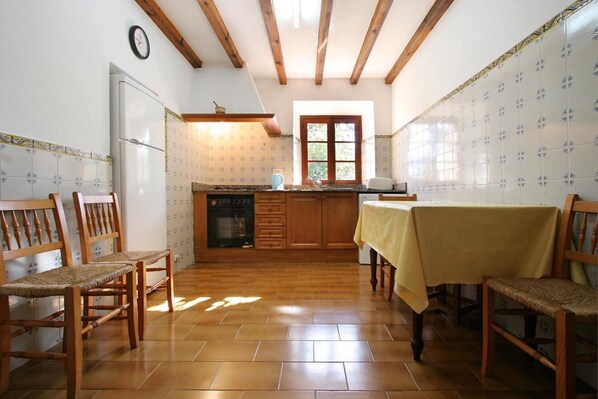 A kitchen with wooden cabinets, a dining table, chairs, a clock, and a window.