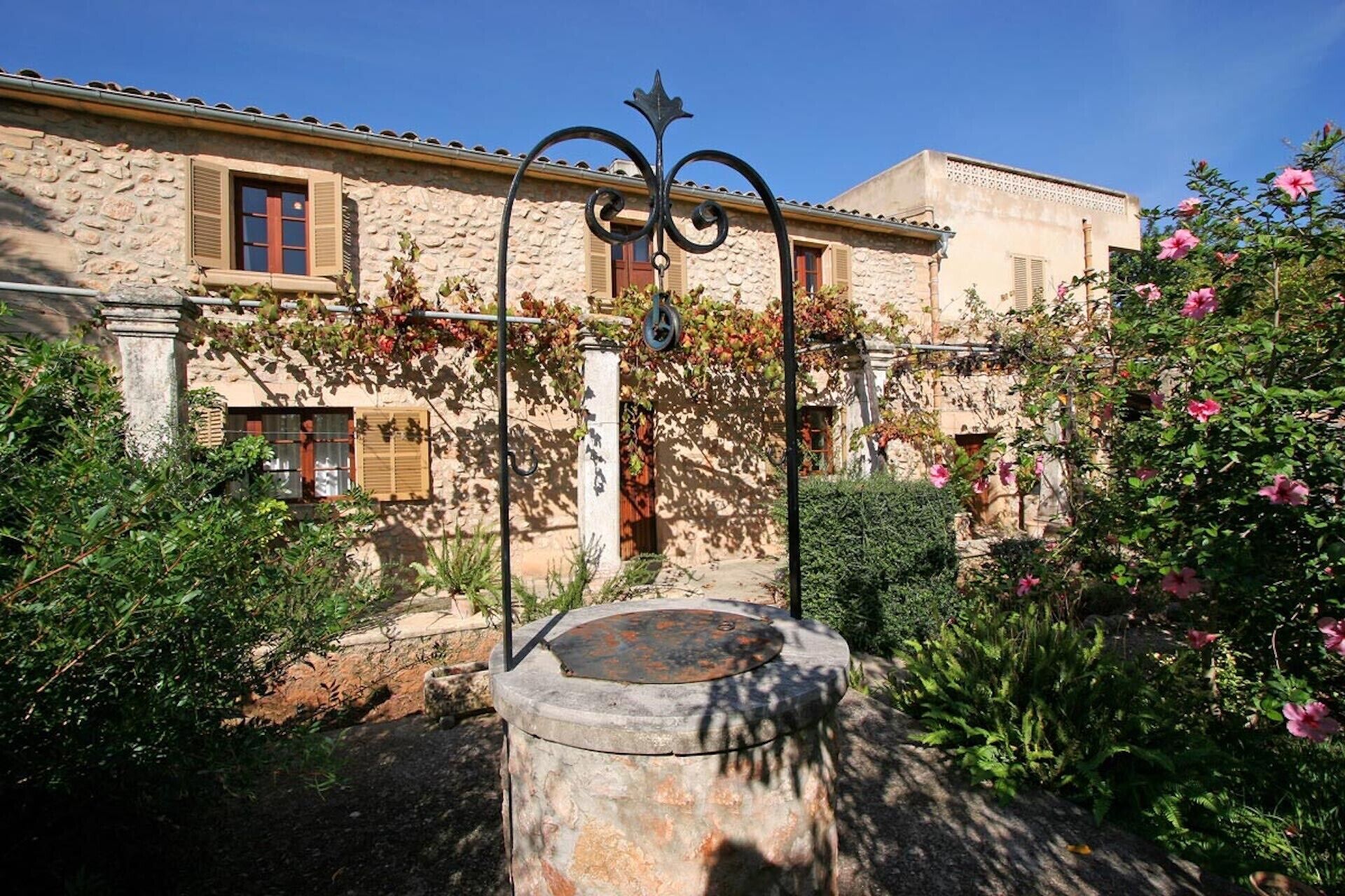 A courtyard with a fountain, stone walls, and flowering plants.