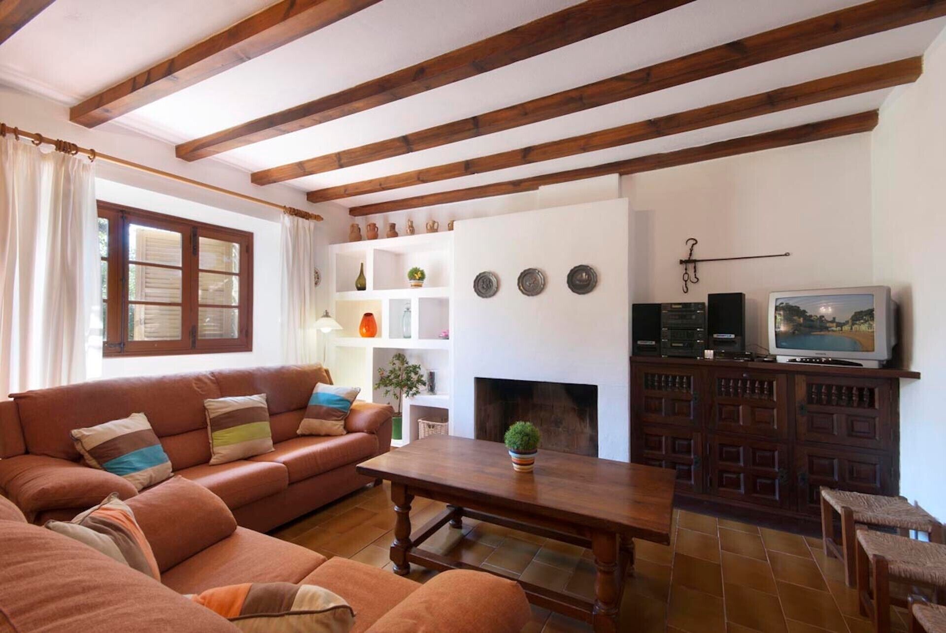 A living room with a sofa, a fireplace, a television, and wooden beams on the ceiling.