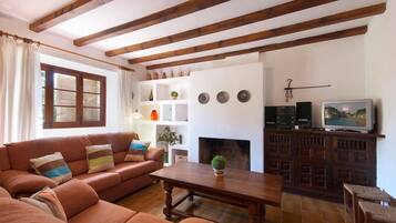 A living room with a sofa, a fireplace, a television, and wooden beams on the ceiling.