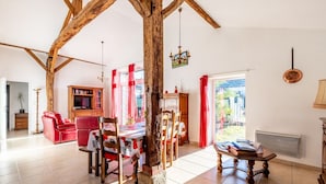 A spacious living room with exposed wooden beams, a dining area with a table and chairs, a red sofa, and a television.