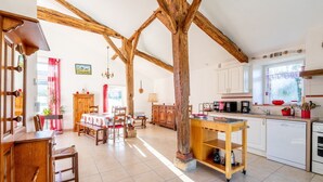 A spacious kitchen with wooden beams, a dining area with a table and chairs, and a view of the outside.