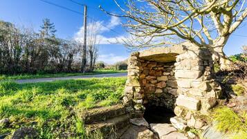 A stone structure with a small opening, surrounded by grass and trees.