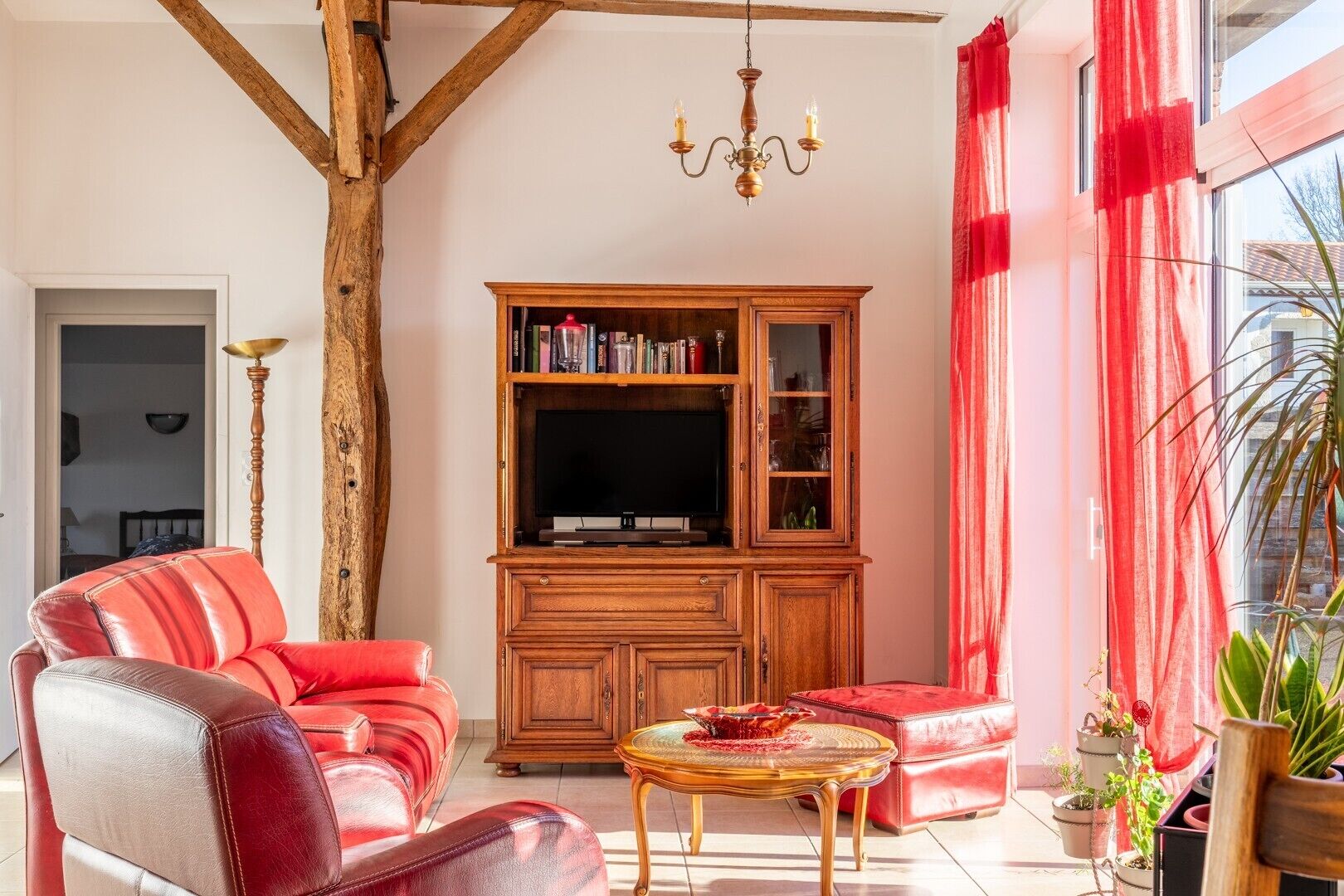 Ein Wohnzimmer mit einem roten Sofa, einem Holzschrank mit Glastüren, einer Chandelieber und Topfpflanzen.