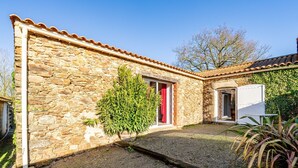 Un bâtiment en pierre avec une porte rouge, un petit arbre et une porte blanche.