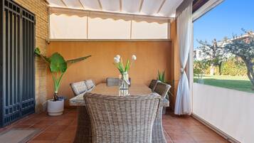 Un patio cubierto con una mesa redonda y sillas de mimbre, una planta en maceta y vistas a un jardín.