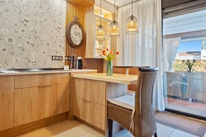 A modern kitchen with wooden cabinetry, a built-in clock, and a dining area with wicker chairs. - Holiday Home 'Emi' with Shared Pool, Wi-Fi & Air Conditioning (Cambrils)