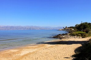 A beach with clear water, a sandy shore, and a house on a hill.