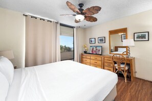 Ein Hotelzimmer mit Bett, Schreibtisch, Stuhl, Deckenventilator und einem Balkon mit Vorhängen.