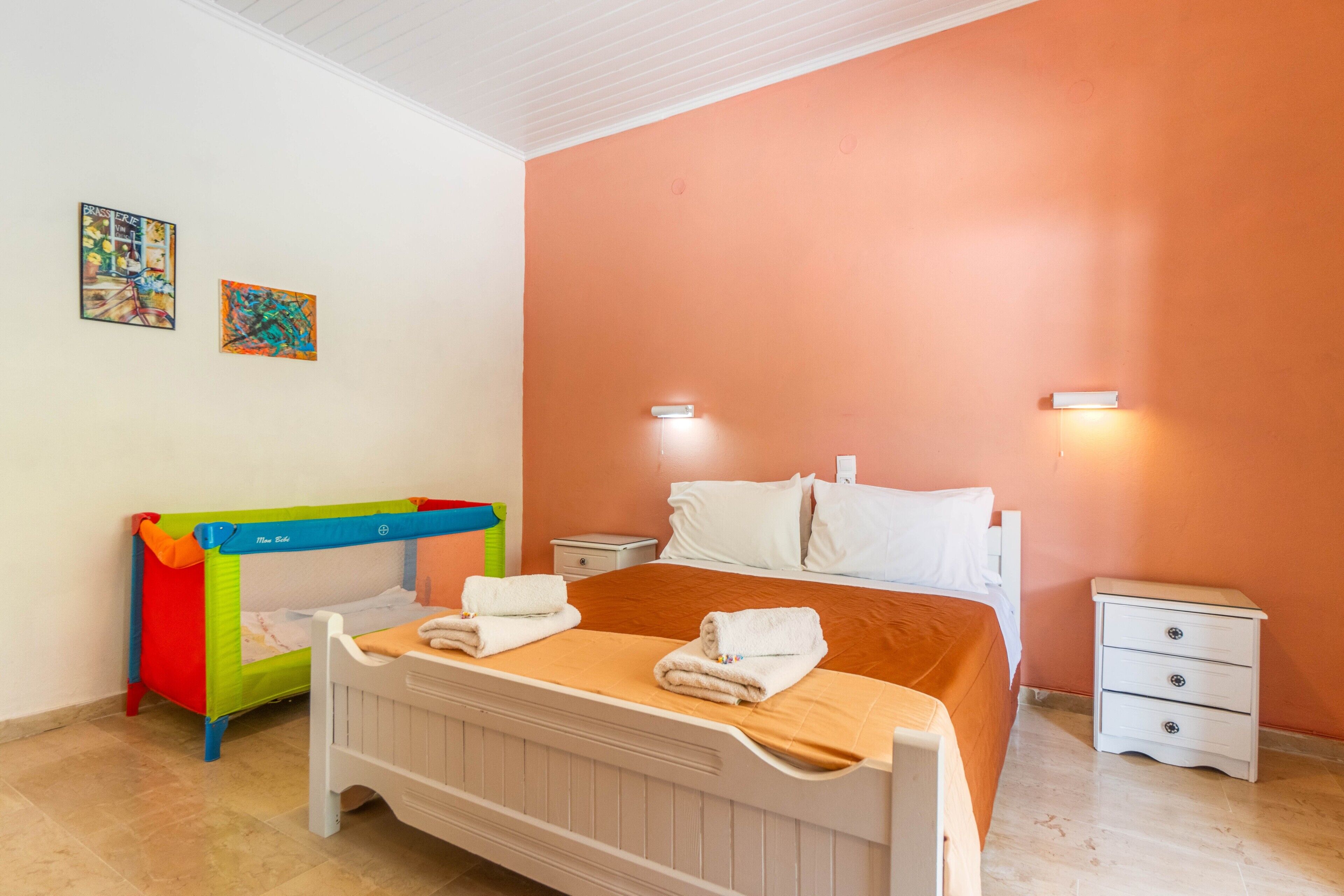 A bedroom with a bed, a crib, a nightstand, and two wall-mounted lights.