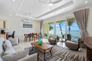 A spacious living area with a dining set, a sofa, and a view of the ocean. - Lovely Cayman Beach Front Villa #2 (Grand Cayman)