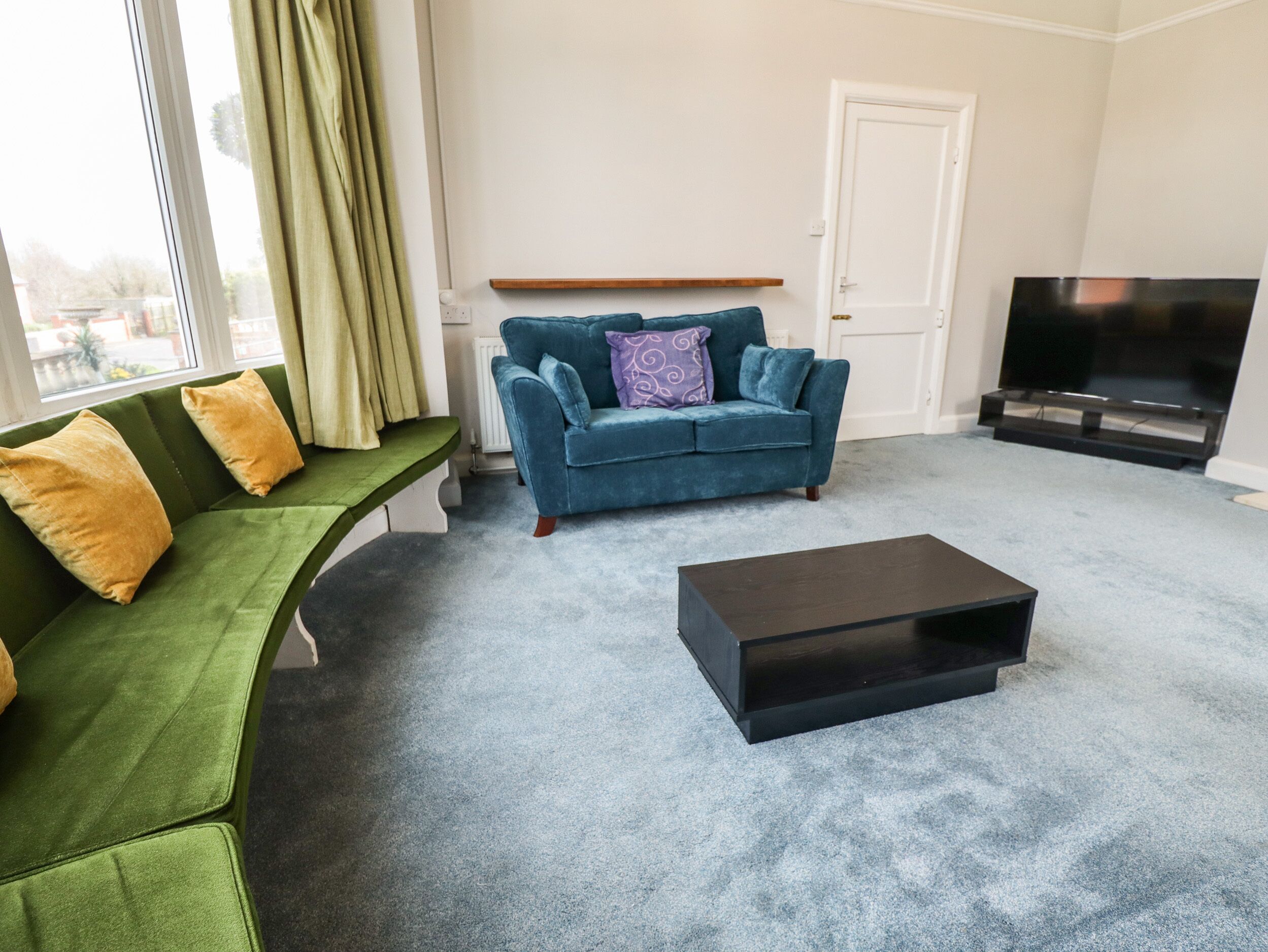 A living room with a green sofa, a blue sofa, a black coffee table, and a TV.