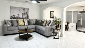 A modern living room with a grey sectional sofa, a round coffee table, a ceiling fan, and a cityscape painting. - Cozy Home 10 minutes from downtown Norcross and 25 minutes from downtown Atlanta (Norcross)