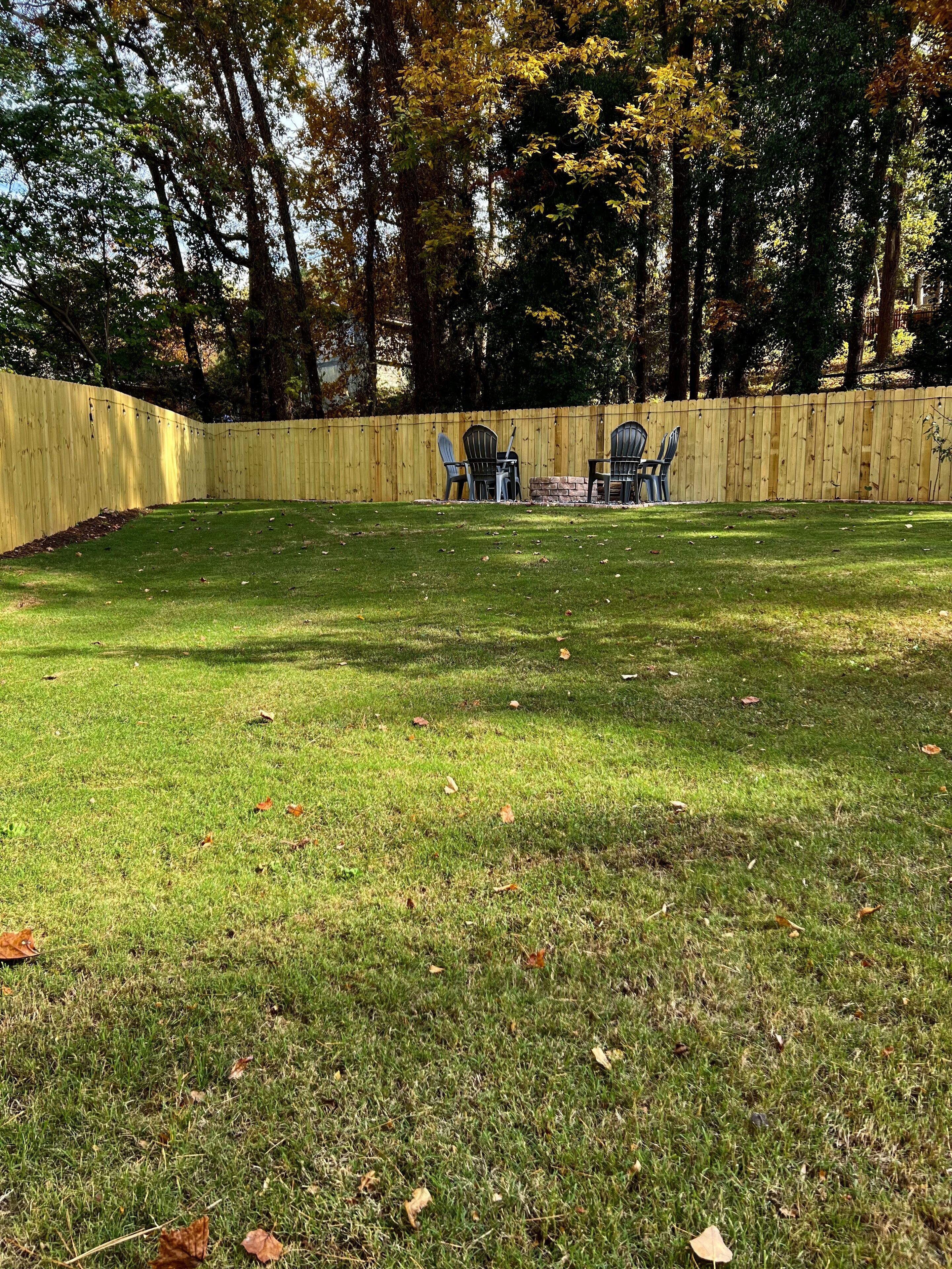 Une cour arrière clôturée avec une pelouse et deux fauteuils Adirondack.
