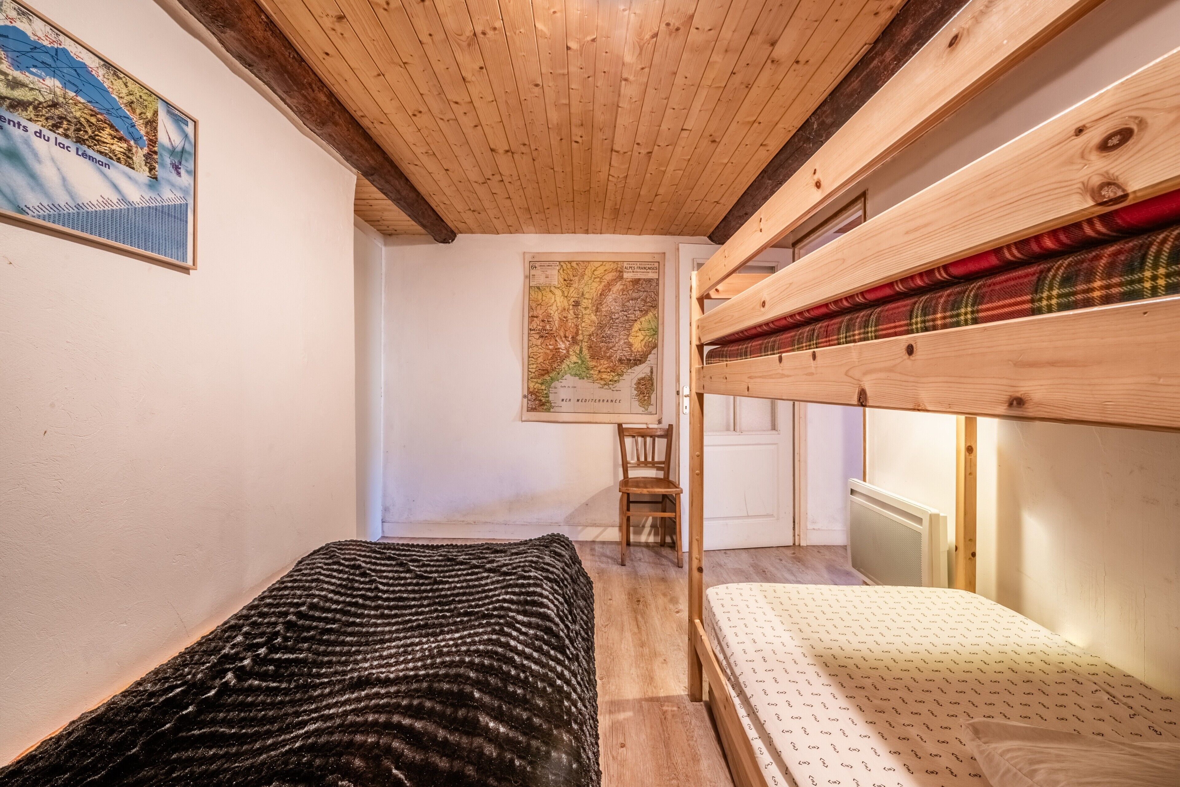 Een kamer met een stapelbed, een eenpersoonsbed, een kaart aan de muur en een stoel.