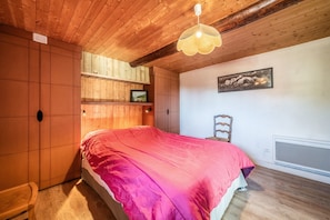 A bedroom with a wooden ceiling, a bed with a pink blanket, a chair, and a wall-mounted picture. - Chalet 'Authentique En Vallée Verte' with Mountain View, Shared Terrace & Wi-Fi (Bogève)