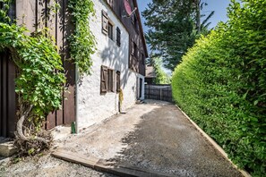 Un étroit sentier de gravier mène à un bâtiment blanc doté de volets en bois et d’une antenne parabolique.