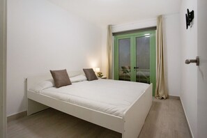 Habitación individual con una puerta verde, una mesita de noche con lámpara y vistas a través de la puerta.