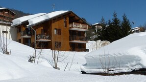 A wooden chalet with balconies, surrounded by snow-covered terrain and trees. - Apartment 'Victorsun2' with Mountain View, Terrace and Private Garden (la clusaz)