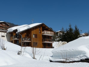 Een houten chalet met balkons, omgeven door besneeuwde vlaktes en bomen.