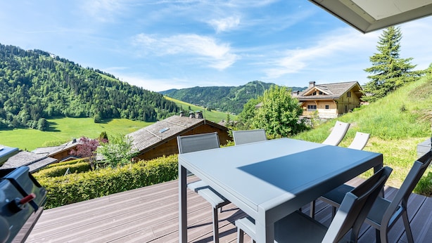 A deck with a table and chairs, overlooking a mountainous landscape with houses. - Apartment 'Victorsun2' with Mountain View, Terrace and Private Garden (la clusaz)