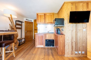 Une cuisine compacte avec des meubles en bois, un four encastré, une télévision et un coin repas comprenant une table et des chaises.