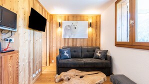 A room with wooden walls, a mounted TV, a sofa with animal-themed cushions, and a large painting of a wolf. - Apartment 'Victorsun2' with Mountain View, Terrace and Private Garden (la clusaz)