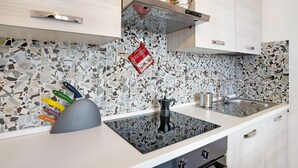 Una cucina con piano cottura nero, lavello e schienale rivestito di mosaici.