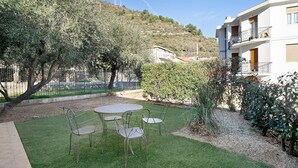 Un cortile con tavolo e sedie, circondato da alberi e un edificio con balconi.