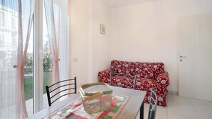 Una stanza con un tavolo da pranzo, una sedia, un divano rosso con motivo floreale e una porta scorrevole in vetro che dà su un giardino.