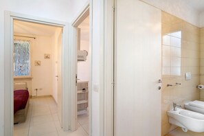 A hotel room with a bed, a bathroom with a bidet, and a hallway leading to another room.