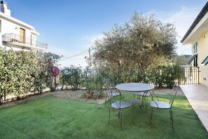 A patio with a round table and chairs, surrounded by a well-maintained lawn and a large tree.