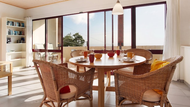 A dining area with wicker chairs, a round table, and a bookshelf.