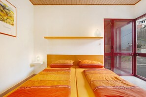 Ein Zimmer mit zwei Betten, einem hölzernen Kopfteil, einem Regal und einer Tür, die auf einen Balkon führt.