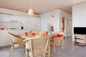 Eine moderne Küche mit weißen Schränken, einem Esstisch mit Korbstühlen und einem Fernsehschrank.