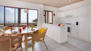 A modern kitchen with white cabinetry, a dining area with wicker chairs, and large windows offering a view.