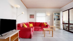 A modern living room with a red sectional sofa, a flat-screen TV, a wooden coffee table, and a bookshelf.