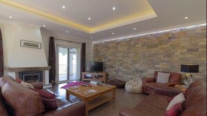 A living room with a fireplace, a television, a stone wall, and leather sofas. - Villa 'Peacehaven' with Mountain View, Wi-Fi and Air Conditioning (Loulé)