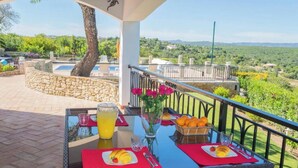 A dining table with a glass of orange juice, a vase with flowers, and a basket of oranges on a balcony overlooking a scenic landscape. - Villa 'Peacehaven' with Mountain View, Wi-Fi and Air Conditioning (Loulé)