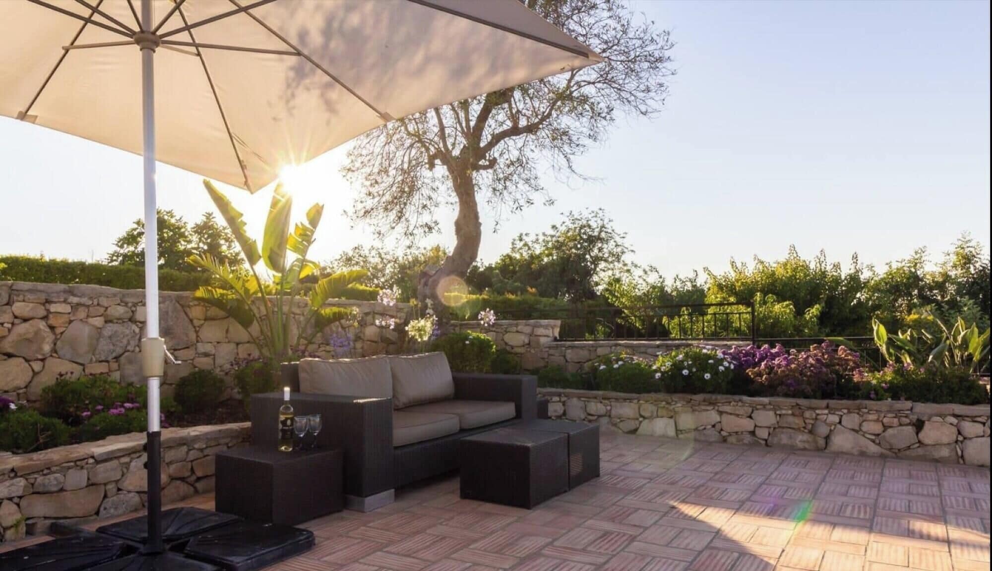 An outdoor seating area with a stone wall, a large umbrella, and a tree.