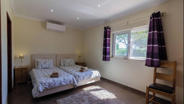 A bedroom with two beds, a window with curtains, a chair, and an air conditioning unit. - Villa 'Peacehaven' with Mountain View, Wi-Fi and Air Conditioning (Loulé)