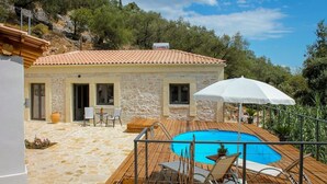 Un bâtiment en pierre avec un toit en tuiles, une piscine et un espace extérieur aménagé pour s’asseoir.